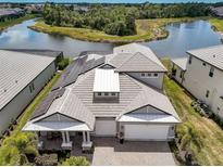 Stunning aerial view of a modern home with solar panels, a gray tile roof, and a serene lake backdrop at 19912 Bridgetown Loop, Venice, FL 34293