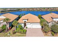 Waterfront home featuring a tile roof, brick driveway, a well-manicured yard, and an attached two car garage at 7036 Whittlebury Trl, Lakewood Ranch, FL 34202