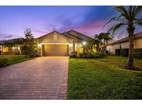 Charming single-Gathering home displaying a two-car garage, brick driveway, and landscaped front yard at twilight at 6912 Gosport Cv, Bradenton, FL 34202
