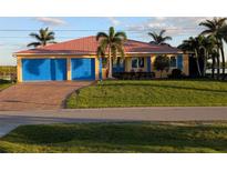 Charming home featuring a well-manicured lawn, a salmon-colored metal roof, and vibrant blue garage doors at 3572 Peace River Dr, Punta Gorda, FL 33983