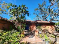 Charming single-story home featuring a beautiful blue door and lush tropical landscaping with palm trees and vibrant plants at 4535 San Siro Dr, Sarasota, FL 34235