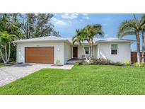 Charming single-story home with a well-manicured lawn, modern wood garage door, and lush tropical landscaping at 6136 Hollywood Blvd, Sarasota, FL 34231