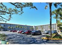 View of a parking lot in front of a light grey condo building with multiple palm trees and bright blue skies at 3108 Lake Bayshore Dr # 211, Bradenton, FL 34205