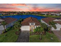 Aerial view of waterfront home with terra cotta roof, brick driveway, lush landscaping, and beautiful sunset at 13228 Saw Palm Creek Trl, Lakewood Ranch, FL 34211