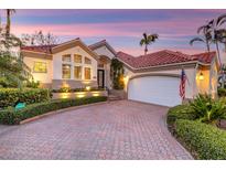 Beautiful home exterior with lush landscaping, brick driveway, and warm exterior lighting at twilight at 612 Weston Pointe Ct, Longboat Key, FL 34228