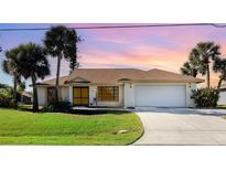 Charming single-story home with a manicured lawn, mature palm trees and a two-car garage with beautiful sunset sky backdrop at 31 Bunker Rd, Rotonda West, FL 33947