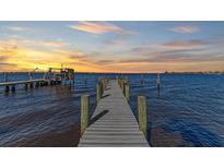 Long wooden dock extends into serene waters, featuring mooring posts, boat lift, and a picturesque sunset backdrop at 2512 Riverside E Dr, Bradenton, FL 34208