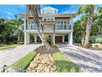 Stunning two-story coastal home featuring lush tropical landscaping and a brick paver driveway at 516 Kumquat Dr, Anna Maria, FL 34216