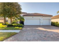 Charming home featuring a three-car garage, red tile roof, beautiful landscaping, and a brick paver driveway at 13145 Amerigo Ln, Venice, FL 34293
