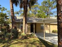 Single-story home with tan exterior, carport, and mature tropical landscaping in a sunny locale at 4933 Village Gardens Dr # 211, Sarasota, FL 34234
