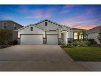 Beautiful single-Gathering home featuring a three-car garage, manicured lawn, and elegant exterior lighting at sunset at 17108 Harvest Moon Way, Bradenton, FL 34211