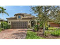 Charming home exterior with a well-maintained lawn, brick driveway, mature tree, and two-car garage in a tranquil setting at 17440 Hampton Falls Ter, Bradenton, FL 34202
