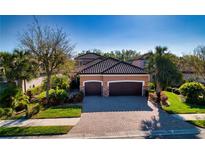Charming home featuring a well-manicured lawn, mature landscaping, and a three-car garage with a tile roof at 9902 Craftsman Park Way, Palmetto, FL 34221