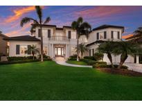 A luxurious two-story home featuring a well-manicured lawn, mature palms, and elegant architectural details at sunset at 348 W Royal Flamingo Dr, Sarasota, FL 34236