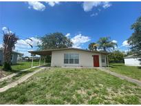 Exterior of a home with neutral paint, carport, small yard, and a bright red front door at 21114 Gladis Ave, Port Charlotte, FL 33952
