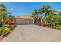 Beautiful home featuring a three-car garage, tile roof, brick paver driveway, and lush tropical landscaping at 8004 River Preserve Dr, Bradenton, FL 34212