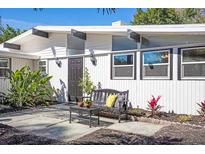 Charming home entrance featuring a cozy bench and black door, enhanced by vibrant landscaping and modern architectural details at 2213 Wason Rd, Sarasota, FL 34231