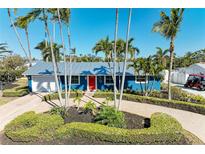 Charming blue single story home boasts lush landscaping, brick driveway, and a vibrant red front door at 502 69Th St, Holmes Beach, FL 34217