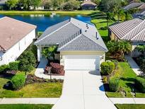 Charming single-story home with a gray roof, well-manicured lawn, and view of a lake at 12717 Deep Blue Pl, Bradenton, FL 34211