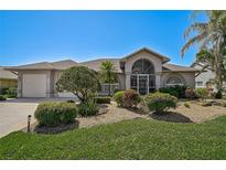 Charming single-story home featuring a well-manicured lawn, tropical plants and a covered entryway with decorative accents at 457 Lake Of The Woods Dr, Venice, FL 34293