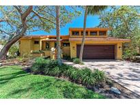 Charming yellow home with a tile roof, lush landscaping, and a brick driveway at 3111 Bayou Sound, Longboat Key, FL 34228