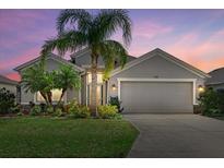 Charming gray home featuring a lush green lawn, mature palms, and a two-car garage under a picturesque sunset sky at 5311 72Nd E St, Palmetto, FL 34221