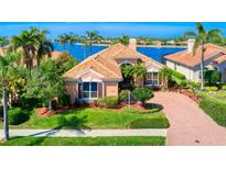 Waterfront home features a tile roof, manicured lawn, lush landscaping, and a brick driveway at 6605 Waters Edge Way, Lakewood Ranch, FL 34202