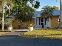 Charming yellow home featuring a metal roof, tropical landscaping, and a welcoming front entrance at 7036 Clark Rd, Sarasota, FL 34241