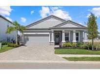 Beautiful single-story home with a brick paved driveway, grey exterior and well-manicured landscaping at 17676 Savory Mist Cir, Bradenton, FL 34211