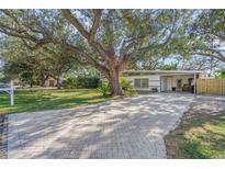 Charming single-story home featuring a beautifully landscaped front yard with mature trees and a brick-paved driveway at 3526 Austin St, Sarasota, FL 34231