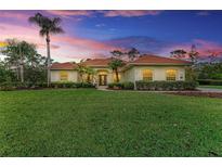 Inviting single-story home with a vibrant green lawn, mature trees, and well-manicured landscaping under a beautiful sunset sky at 22333 Panther Loop, Bradenton, FL 34202