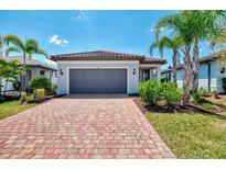 Charming home featuring a red brick driveway, gray garage door, and manicured landscaping with lush bushes at 17714 Northwood Pl, Bradenton, FL 34202