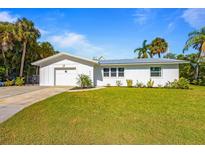 Charming single-story home featuring a lush front lawn, pristine white exterior, and a convenient attached garage at 414 79Th St, Holmes Beach, FL 34217