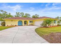 Charming yellow home featuring a large driveway, manicured lawn, and bright blue arched front door and shutters at 2909 Concord St, Sarasota, FL 34231