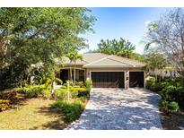 Charming single-story home with a tile roof, lush landscaping, and a brick paver driveway leading to a three-car garage at 4915 Old Tree Pl, Sarasota, FL 34233