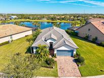 Stunning aerial view of a lakeside home with a beautiful tile roof, brick driveway, and lush landscaping at 5590 Rain Lily Ct, Sarasota, FL 34238