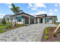 Modern home with a paver driveway, three-car garage, and meticulously landscaped front yard with palm tree at 800 Blue Shell Loop, Sarasota, FL 34240
