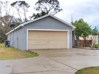 Detached one-car garage featuring a light-beige door and concrete driveway, surrounded by a well-maintained lawn and mature trees at 2309 30Th W Ave, Bradenton, FL 34205