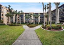 Well-maintained building exterior with lush landscaping and a welcoming walkway surrounded by mature palms at 3006 Caring Way # 210, Port Charlotte, FL 33952