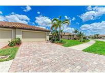 Beautiful home featuring brick paver driveway, two-car garage, and lush landscaping with blue sky in the background at 19889 Benissimo Dr, Venice, FL 34293