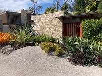 Beautiful landscaping with stone accent wall, wood pergola, and tropical plants adorns the front of this home at 4408 Midnight Pass Rd, Sarasota, FL 34242