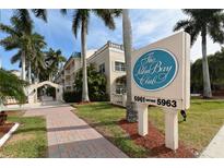 The Palm Bay Club condo community featuring lush landscaping, a paver walkway, and exterior signage at 5963 Midnight Pass Rd # 355, Sarasota, FL 34242