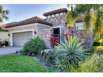 Charming home featuring a stone facade, tile roof, well-manicured landscaping, and a welcoming entrance gate at 9914 Craftsman Park Way, Palmetto, FL 34221