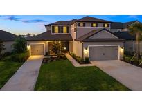 Charming two-story home featuring a manicured lawn and a three-car garage with individual doors at twilight at 16626 Paynes Mill Dr, Lakewood Ranch, FL 34211