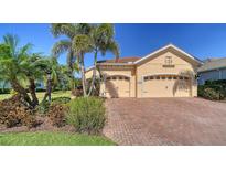 Charming home featuring a brick driveway, two-car garage, and lush tropical landscaping with palm trees at 21287 Sandal Foot Dr, Venice, FL 34293