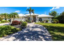 Inviting single-story home with a paver driveway, lush landscaping, and a pristine white tile roof at 832 Carnoustie Dr, Venice, FL 34293
