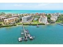 Stunning aerial view of beachfront condos, a pier, and boats on the sparkling turquoise waters of the Gulf at 8701 Midnight Pass Rd # 206A, Sarasota, FL 34242