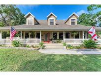 Charming home with three dormers, covered porch with white railing, American and Florida flags, and lush lawn at 906 134Th E St, Bradenton, FL 34212