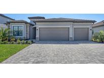 Two car garage with grey doors and stone veneer accents, set in a gray home with a paved driveway at 15332 Serene Shores Loop St, Bradenton, FL 34211