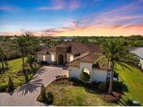 Stunning aerial view of a single-Gathering home with lush landscaping, brick driveway, and barrel tile roof at sunset at 26725 Raphis Royale Blvd, Englewood, FL 34223